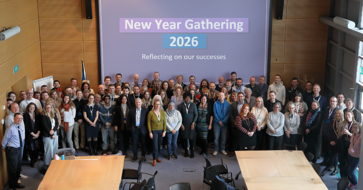 Revenue Scotland staff assembled in a conference room. Text on the screen behind them reads "New Year Gathering 2026"